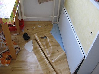 Vyhrabané a místy potrhané tenké lino zpod úzké skříňky na uložení mnoha krabic s 
mlékem
